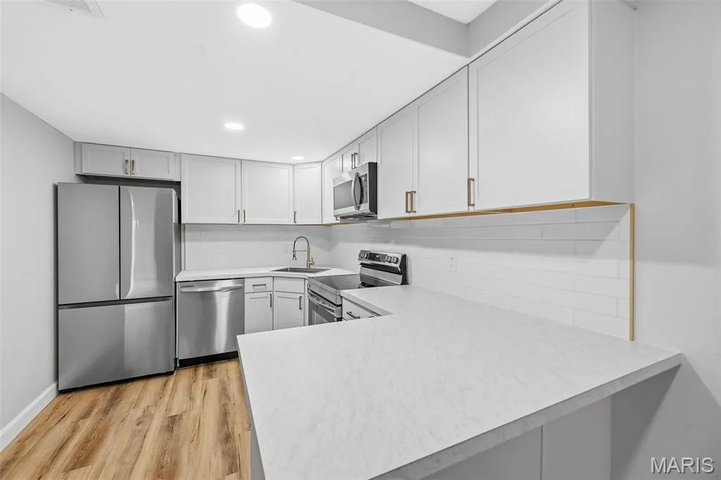 Kitchen featuring recessed lighting, light-toned cabinetry, stainless steel appliances, a white subway tile backsplash, and wood-finish LVP flooring — 1410 Heritage Landing #106, St Charles, MO 63303
