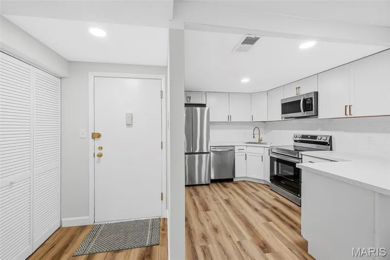 White cabinetry and countertops with stainless steel appliances, wood-finish flooring, and white louvered bifold doors — 1410 Heritage Landing #106, St Charles, MO 63303