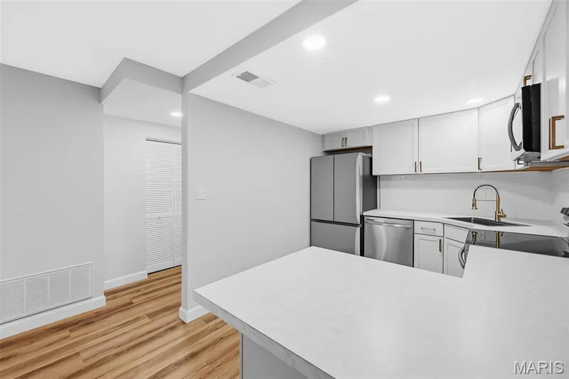 Kitchen featuring white cabinetry, stainless steel appliances, white countertops, and wood-finish flooring — 1410 Heritage Landing #106, St Charles, MO 63303