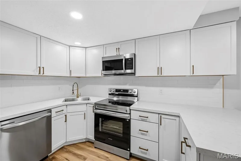 White shaker-style cabinetry with gold-finish hardware, stainless steel appliances, light-toned countertops, white subway tile backsplash, and wood-finish flooring — 1410 Heritage Landing #106, St Charles, MO 63303