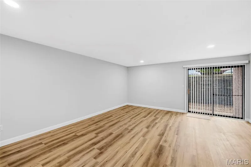 Spacious room featuring wood-finish flooring, light gray walls, recessed lighting, and a sliding glass door with vertical blinds — 1410 Heritage Landing #106, St Charles, MO 63303