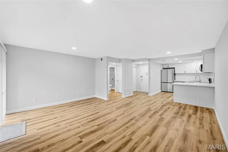 Expansive living area featuring wood-finish flooring, recessed lighting, and a modern kitchen with stainless steel appliances — 1410 Heritage Landing #106, St Charles, MO 63303