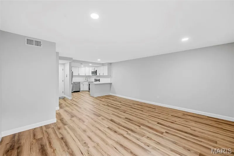 Spacious open-concept layout with wood-finish flooring, recessed lighting, and a kitchen featuring white cabinetry, stainless steel appliances, and a breakfast bar — 1410 Heritage Landing #106, St Charles, MO 63303