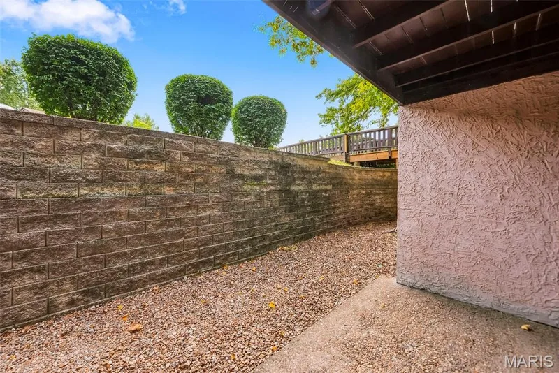 Retaining wall with integrated shrubbery, gravel ground cover, textured exterior wall, and concrete patio section — 1410 Heritage Landing #106, St Charles, MO 63303