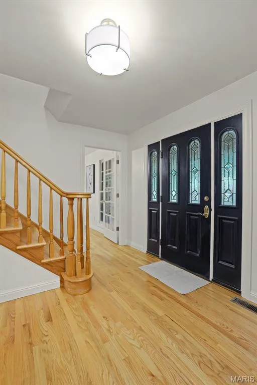 Entryway featuring wood-finish flooring, a multi-panel door with decorative glass inserts, and a staircase with a natural-finish wooden banister and spindles — 229 Quail Run Drive, Defiance, MO 63341