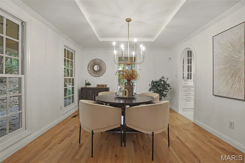 Dining area featuring a tray ceiling, wood-finish flooring, multi-light chandelier, multi-pane windows, and an arched entryway with built-in cabinetry — 229 Quail Run Drive, Defiance, MO 63341