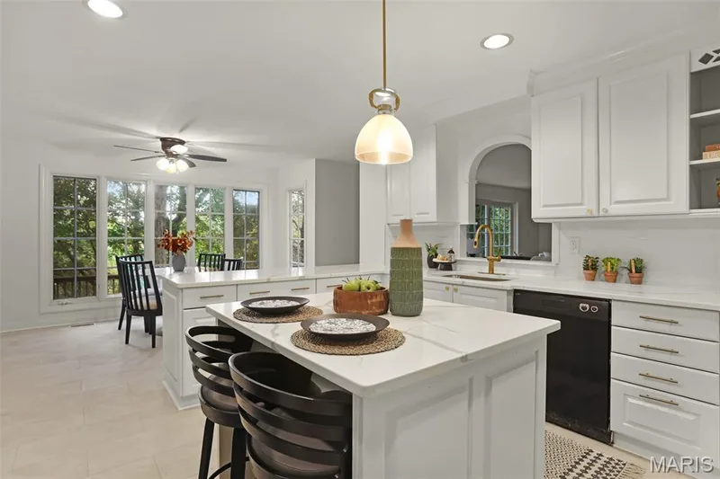 Kitchen featuring white cabinetry, center island with stone-finish countertop, recessed lighting, brass-finish faucet, and arched decorative wall opening — 229 Quail Run Drive, Defiance, MO 63341