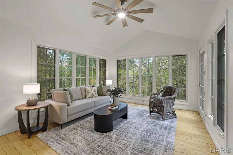 Vaulted ceiling with an integrated multi-blade ceiling fan, expansive grid-pane windows, and light-tone wood-finish flooring — 229 Quail Run Drive, Defiance, MO 63341