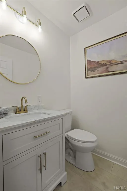 Shaker-style vanity with stone-top basin, metallic-finish faucet, circular wall mirror, and three-light vanity fixture — 229 Quail Run Drive, Defiance, MO 63341