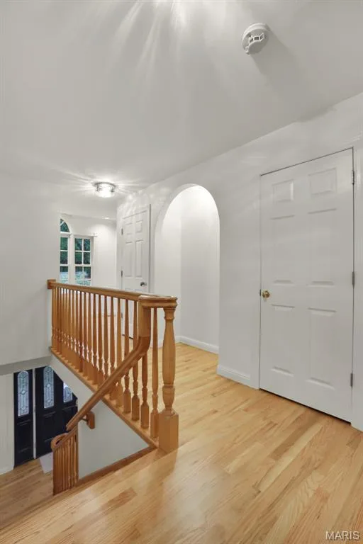 Upper landing featuring wood-finish flooring, a traditional wood spindle railing, arched architectural detailing, and six-panel interior doors — 229 Quail Run Drive, Defiance, MO 63341
