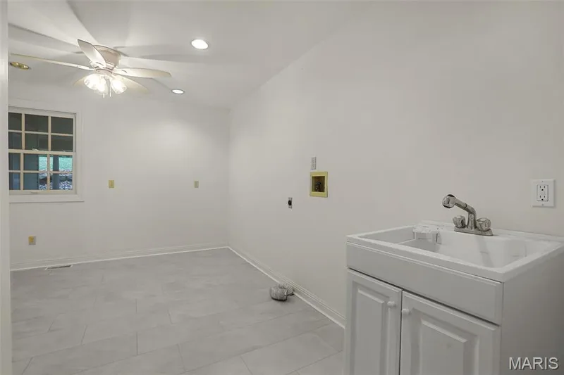 Utility room featuring large-format ceramic tile flooring, a built-in white vanity cabinet with a drop-in basin, a chrome faucet, a multi-pane window, and a ceiling fan with integrated lighting — 229 Quail Run Drive, Defiance, MO 63341