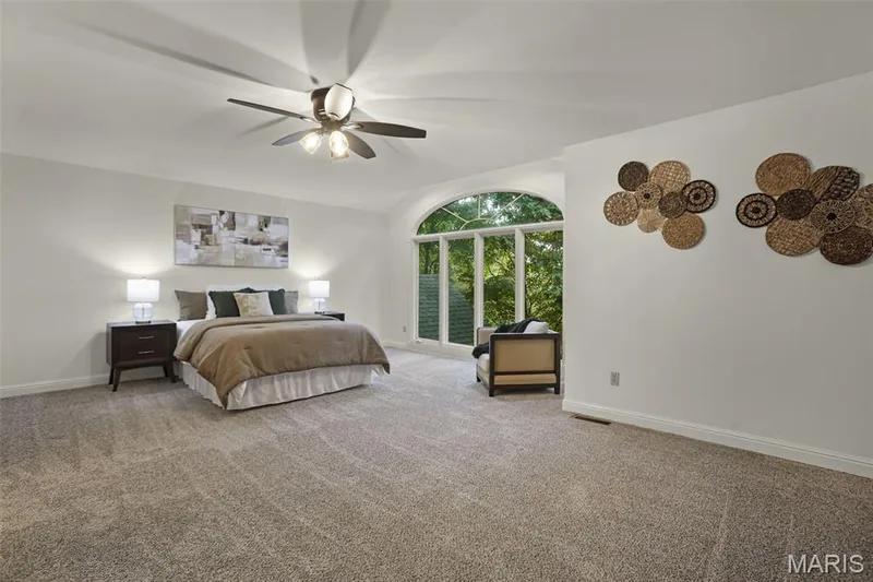 Arched window featuring floor-to-ceiling glass panes, neutral wall-to-wall carpeting, and a multi-blade ceiling fan with an integrated light fixture — 229 Quail Run Drive, Defiance, MO 63341