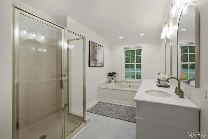 Bathroom featuring a glass-enclosed shower, dual-sink vanity with metallic fixtures, inset soaking tub, and arched mirrors — 229 Quail Run Drive, Defiance, MO 63341