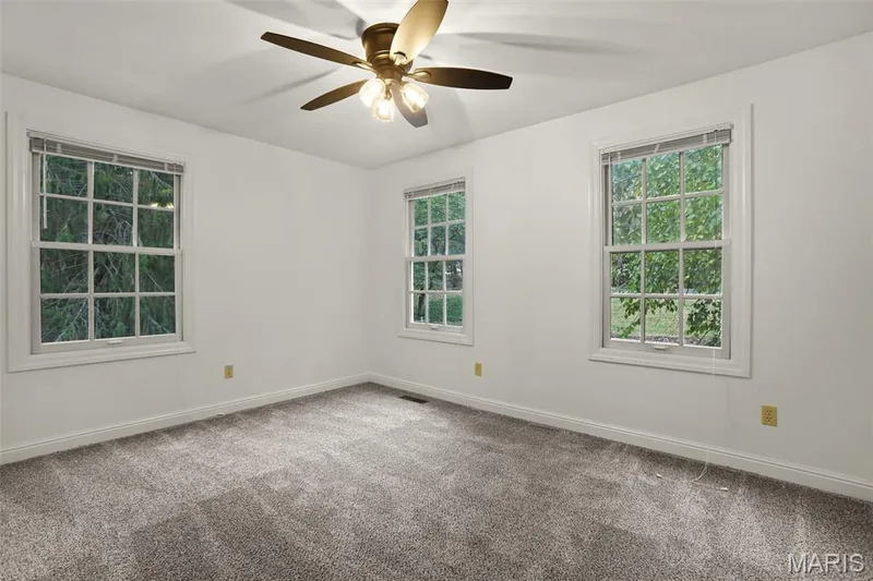 Neutral-toned wall-to-wall carpeting, three multi-pane windows with white trim, and a ceiling fan with integrated light fixtures — 229 Quail Run Drive, Defiance, MO 63341