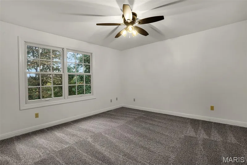 Neutral-toned interior space featuring wall-to-wall carpeting, multi-pane windows, and a ceiling-mounted light fixture with a five-blade fan — 229 Quail Run Drive, Defiance, MO 63341