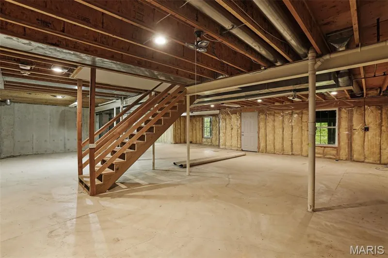 Unfinished space featuring a concrete floor, exposed wood joist ceiling, wooden staircase, insulated wall panels, and two windows — 229 Quail Run Drive, Defiance, MO 63341