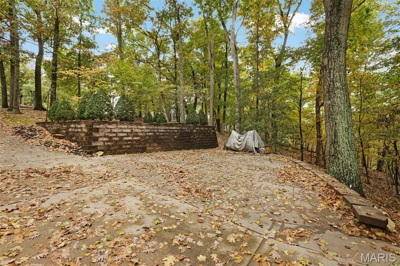 Flagstone patio featuring a stone masonry retaining wall and mature woodland surroundings — 229 Quail Run Drive, Defiance, MO 63341