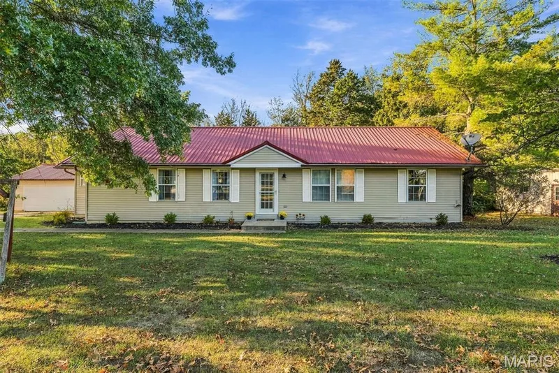 Single-story residence featuring light-toned horizontal siding, a red metal roof, symmetrical white shutters, and a detached garage — 10341 Rose Lane, Foristell, MO 63348