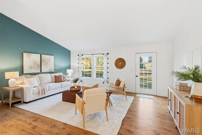 Living area featuring a vaulted ceiling, wood-finish flooring, a large accent wall, dual windows, and an exterior door with glass panes — 10341 Rose Lane, Foristell, MO 63348