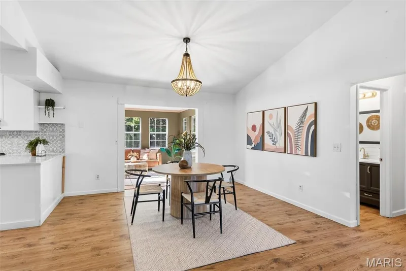 Open-concept space featuring wood-finish flooring, a vaulted ceiling, bead-draped chandelier lighting, and patterned tile backsplash — 10341 Rose Lane, Foristell, MO 63348