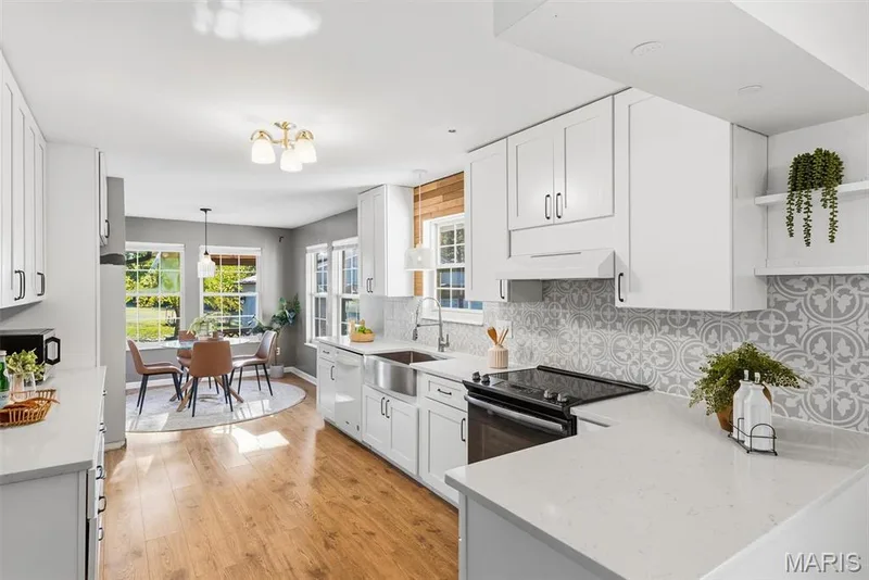 Kitchen featuring white cabinetry, quartz countertops, a farmhouse-style sink, patterned tile backsplash, and wood-finish flooring — 10341 Rose Lane, Foristell, MO 63348