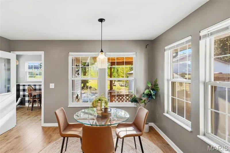 Kitchen eating area featuring wood-finish flooring, neutral wall tones, large double-hung windows with colonial grilles, and a single glass pendant light fixture — 10341 Rose Lane, Foristell, MO 63348