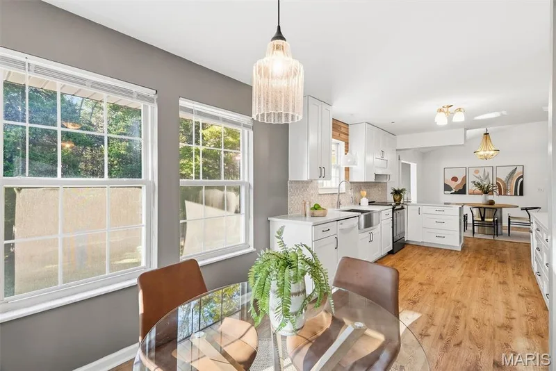 Kitchen featuring white shaker-style cabinetry, wood-finish flooring, a farmhouse sink, and a decorative textured tile backsplash, illuminated by a cylindrical glass pendant light — 10341 Rose Lane, Foristell, MO 63348
