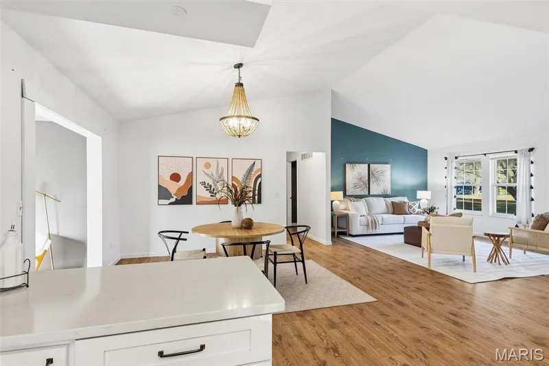 Open-concept interior featuring vaulted ceilings, wood-finish flooring, a decorative chandelier, and a prominent accent wall — 10341 Rose Lane, Foristell, MO 63348