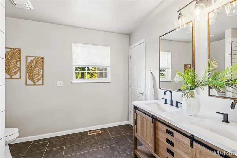Primary Bathroom featuring a dual-sink vanity with a white countertop and sliding barn-door cabinet fronts, matte black fixtures, large rectangular mirrors, and tile flooring — 10341 Rose Lane, Foristell, MO 63348