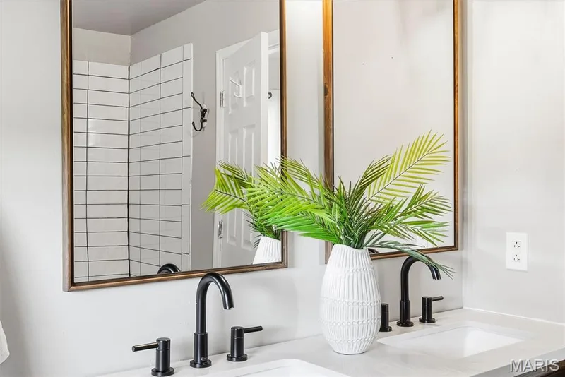 Primary Dual vanity featuring rectangular undermount sinks, stone countertops, matte black widespread faucets, and wood-framed mirrors, with a subway-tiled shower surround — 10341 Rose Lane, Foristell, MO 63348
