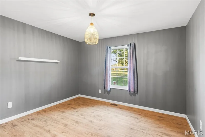 Bedroom featuring wood-finish flooring, grey walls, a built-in wall-mounted shelf, a single-hung window, and a textured pendant light fixture — 10341 Rose Lane, Foristell, MO 63348
