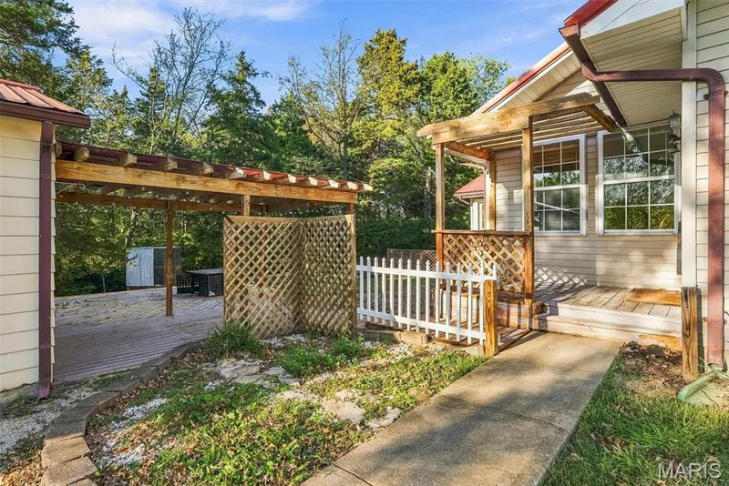 Exterior living space featuring a multi-level wood deck, pergola structures, wood lattice privacy screens, and a concrete pathway — 10341 Rose Lane, Foristell, MO 63348
