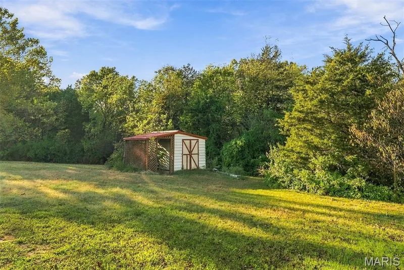 Expansive grounds featuring a grass lawn, storage shed, attached lattice-work enclosure, and mature perimeter trees — 10341 Rose Lane, Foristell, MO 63348