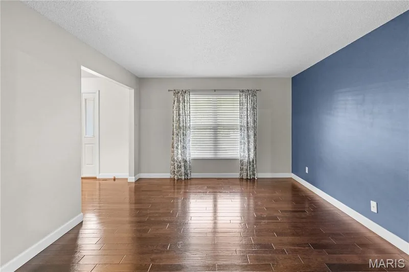 Living area featuring wood-finish flooring, a bold blue accent wall, neutral wall tones, and a window with horizontal blinds — 838 Emerald Place Drive, St Charles, MO 63304