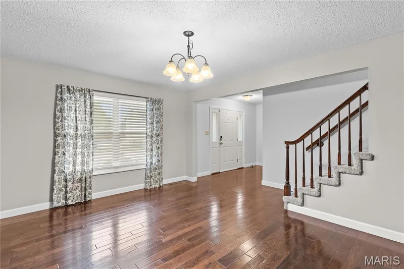Interior space featuring wood-finish flooring, a five-arm chandelier, and a staircase with a dark wood handrail and carpeted treads — 838 Emerald Place Drive, St Charles, MO 63304