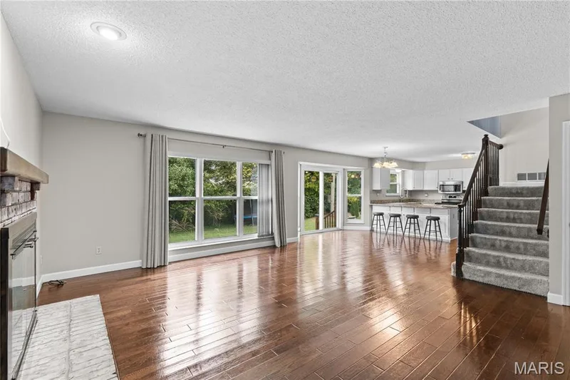 Open-concept living space featuring wood-finish flooring, a fireplace with a brick surround, a sliding glass door, and a built-in kitchen island — 838 Emerald Place Drive, St Charles, MO 63304