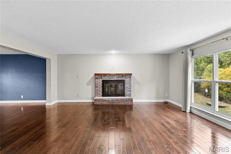 Living area featuring wood-finish flooring, brick fireplace with a wood mantel, and large windows — 838 Emerald Place Drive, St Charles, MO 63304