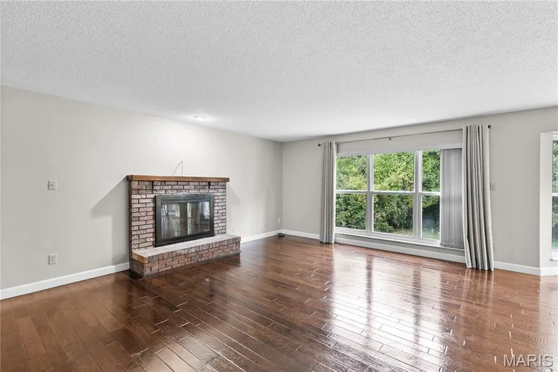 Living area featuring wood-finish flooring, brick fireplace with a wood mantel, and large windows — 838 Emerald Place Drive, St Charles, MO 63304