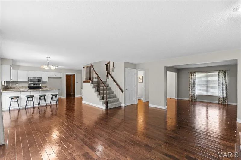 Open-concept interior featuring wood-finish flooring, a kitchen island with stone countertops, a staircase with a wooden handrail, and white cabinetry — 838 Emerald Place Drive, St Charles, MO 63304
