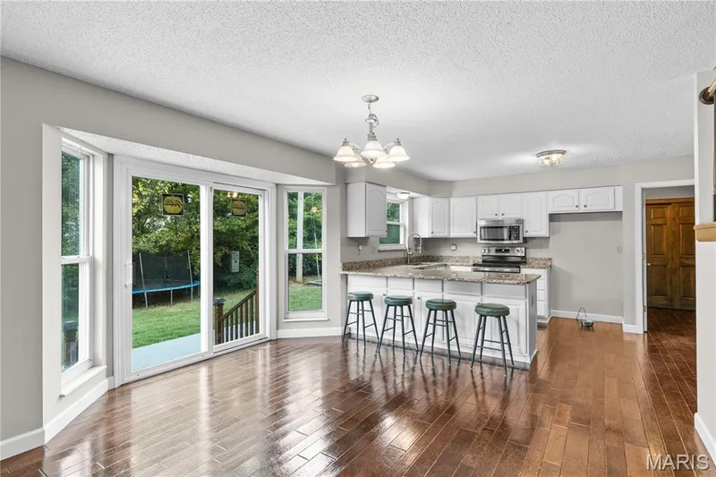 Open-concept kitchen featuring wood-finish flooring, white cabinetry, stone-surfaced countertops, a breakfast bar, and sliding glass doors — 838 Emerald Place Drive, St Charles, MO 63304