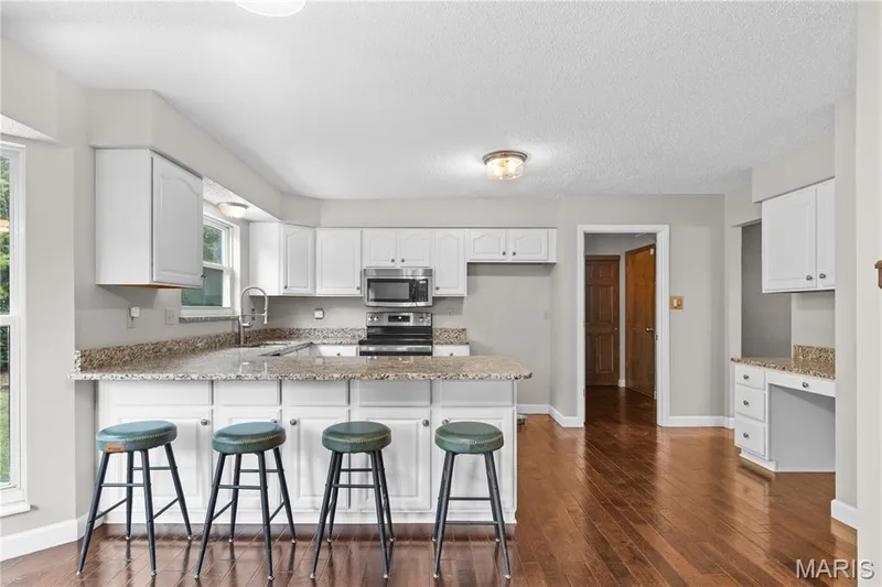 Kitchen featuring white shaker-style cabinetry, stone-finish countertops, stainless steel appliances, a peninsula breakfast bar, and wood-finish flooring — 838 Emerald Place Drive, St Charles, MO 63304