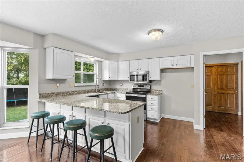 Kitchen featuring white cabinetry, stone-finish countertops, stainless steel appliances, and wood-finish flooring — 838 Emerald Place Drive, St Charles, MO 63304