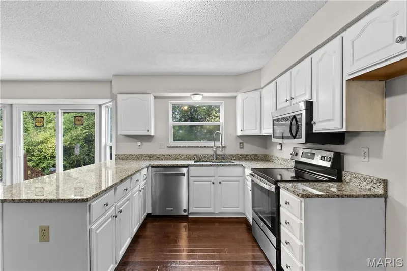 Kitchen featuring white cabinetry, stone-surface countertops, wood-finish flooring, stainless steel appliances, and sliding glass doors — 838 Emerald Place Drive, St Charles, MO 63304