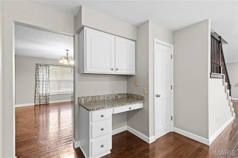 Built-in desk area with white cabinetry, stone-finish countertop, and three-drawer storage, wood-finish flooring, and staircase with dark-finished railings — 838 Emerald Place Drive, St Charles, MO 63304
