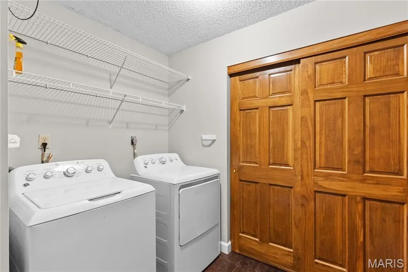Laundry room featuring wood-finish flooring, six-panel wood sliding closet doors, and wall-mounted wire shelving — 838 Emerald Place Drive, St Charles, MO 63304