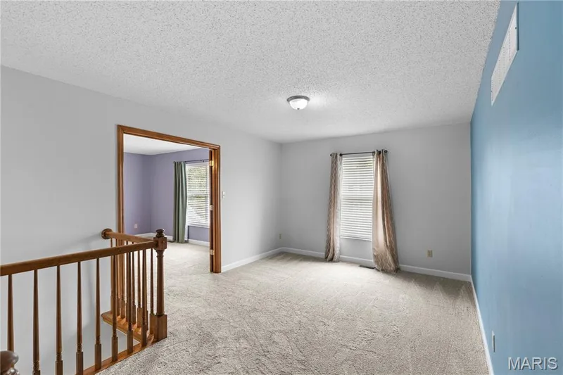 Neutral-toned room featuring a wood-toned balustrade, wall-to-wall carpeting, and a prominent blue accent wall — 838 Emerald Place Drive, St Charles, MO 63304