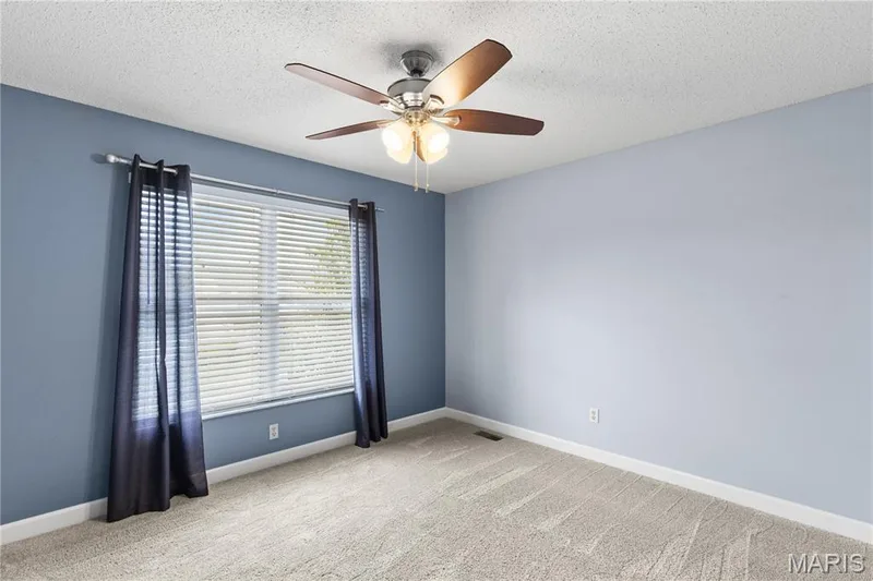 Neutral-toned wall paint, multi-tone carpeting, multi-blade ceiling fan with integrated lighting, and single-hung window with blinds — 838 Emerald Place Drive, St Charles, MO 63304
