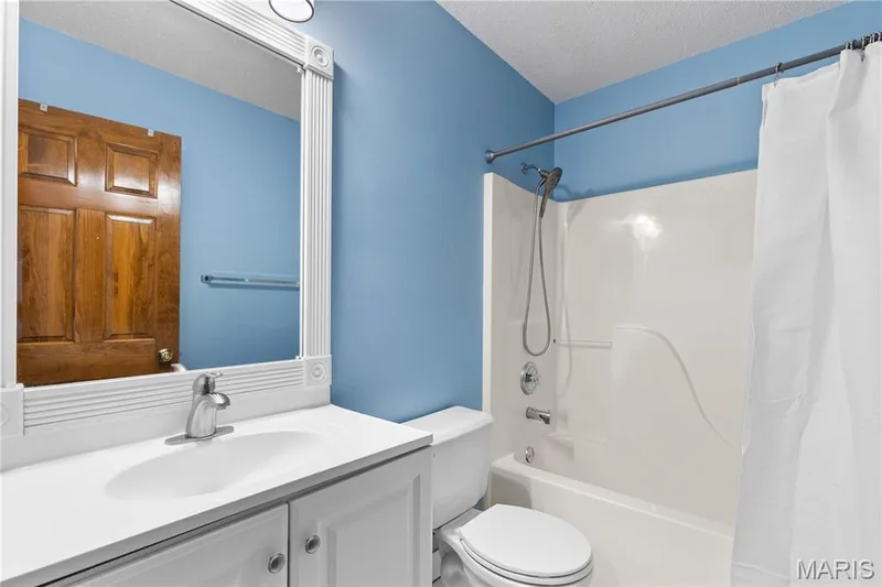White vanity with an integrated basin, framed wall mirror, and a combination bathtub and shower surround with metallic hardware — 838 Emerald Place Drive, St Charles, MO 63304