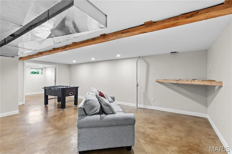 Finished lower level featuring stained concrete flooring, recessed lighting, exposed wood-beam accents, and a built-in wood wall shelf — 838 Emerald Place Drive, St Charles, MO 63304