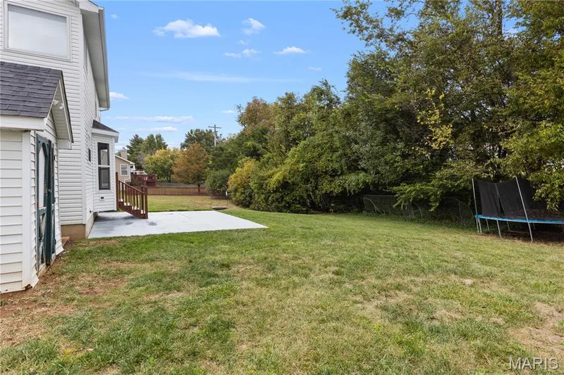 Rear exterior featuring a concrete patio, wood-finish steps, and a spacious lawn area with mature trees — 838 Emerald Place Drive, St Charles, MO 63304